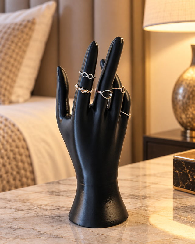 Main porte-bijoux noire dressée, présentant plusieurs bagues sur ses doigts.