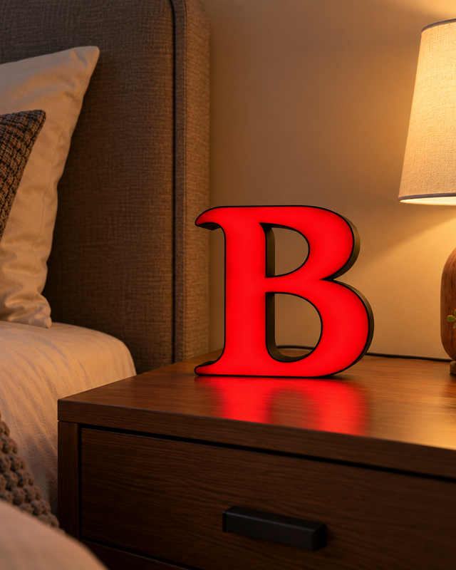 Lettre B lumineuse rouge à contour sombre posée sur une table de chevet.